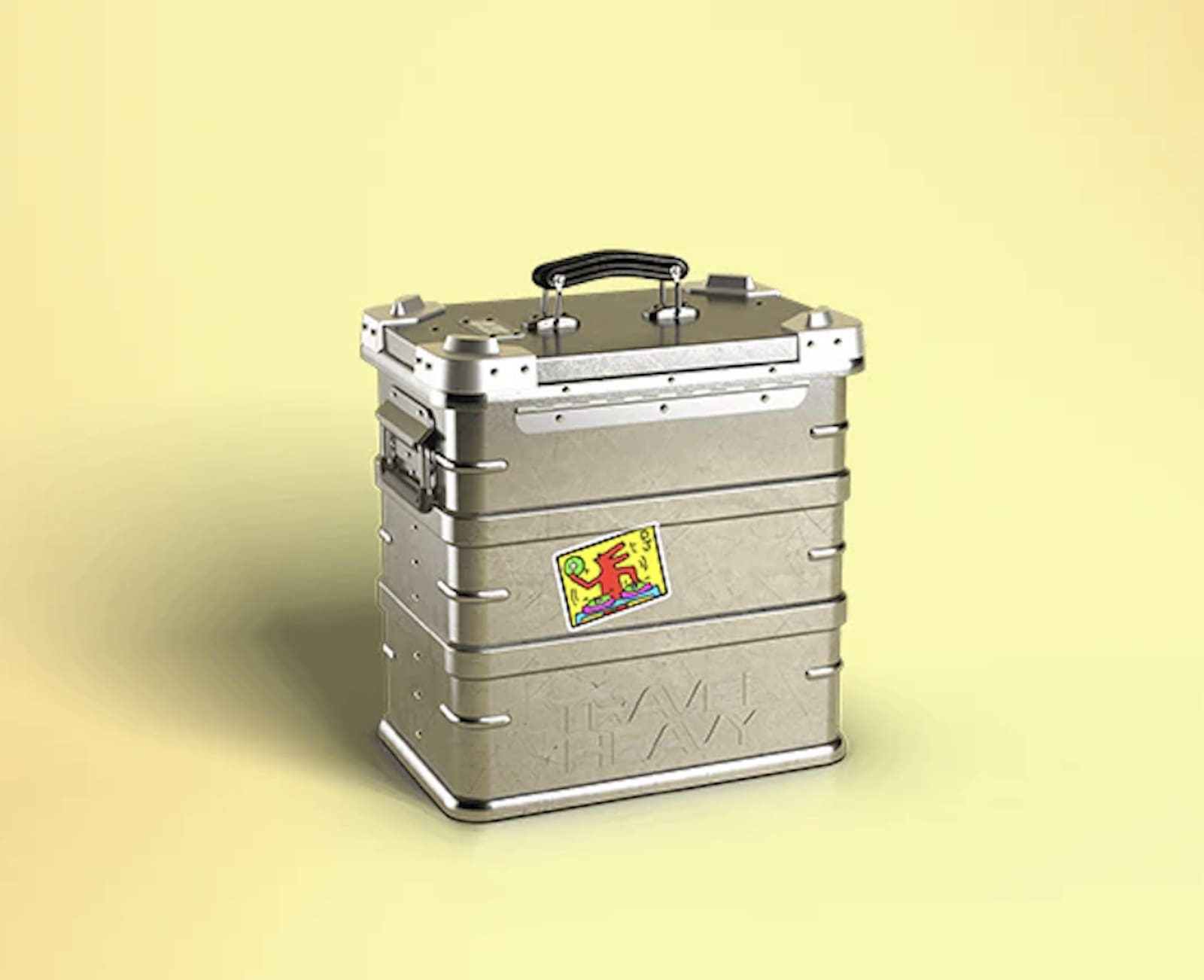 A silver metal record case (Travel Heavy The World’s Toughest 12” Record Case) with a colorful sticker sits against a yellow backdrop