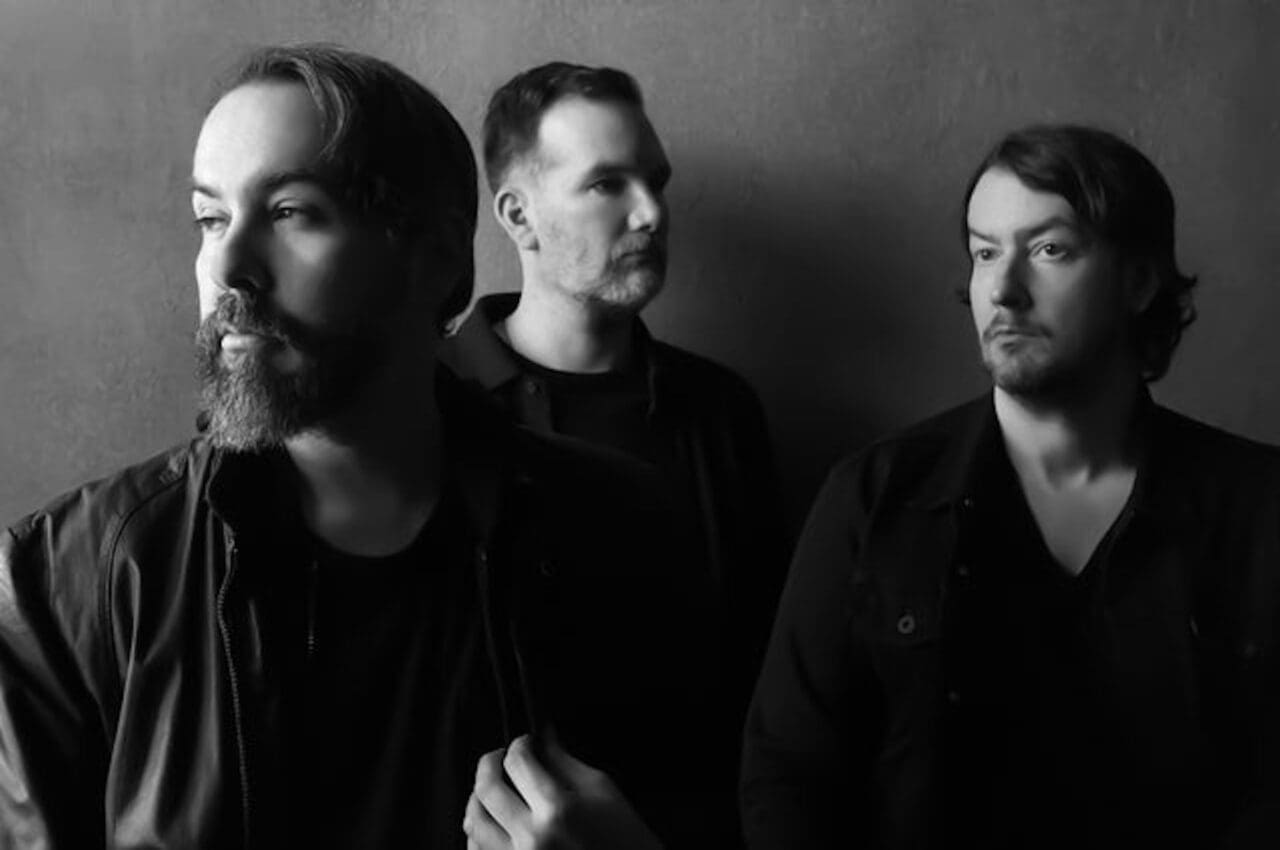 Members of American band Cigarettes After Sex posed in front of a grey background