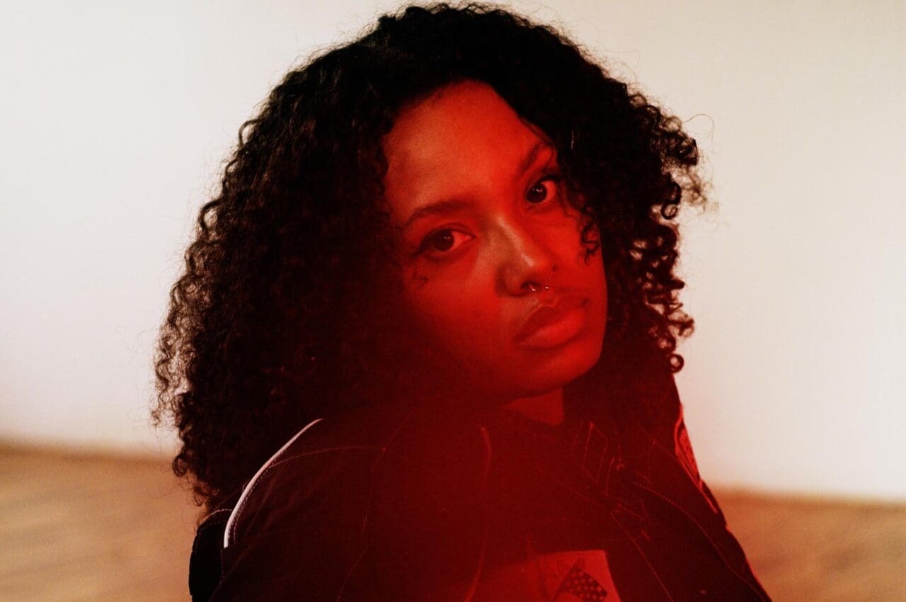 A woman bathed in red light stares at the camera