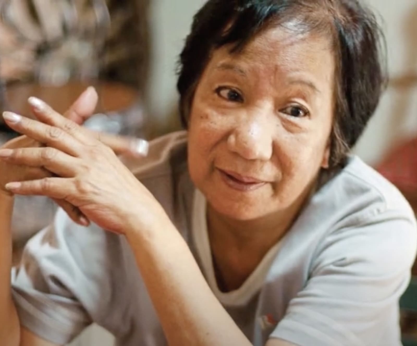 an older woman sits pensively with her hands crossed