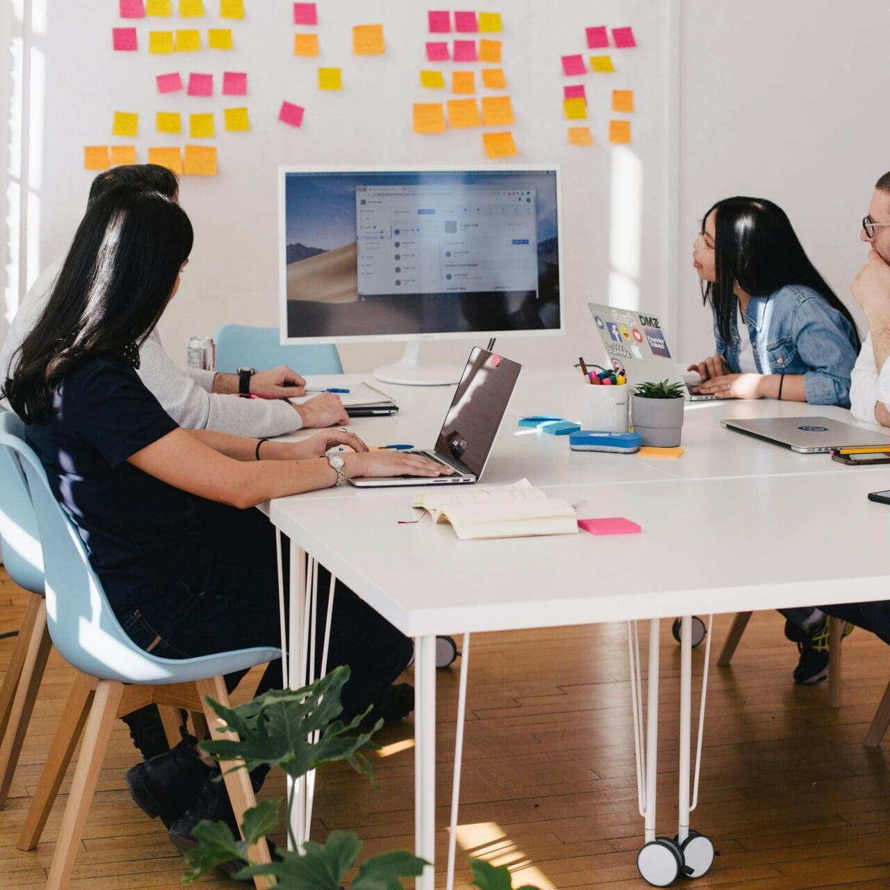 Office workers gather around a white table and look at an iMac