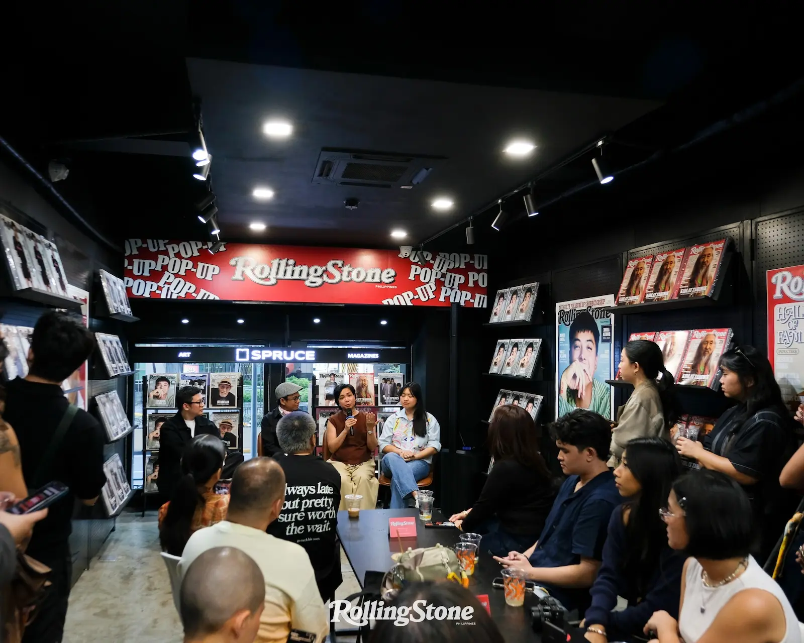 Panel discussion in a Rolling Stone Philippines store, with speakers on a stage and an audience around a long table.