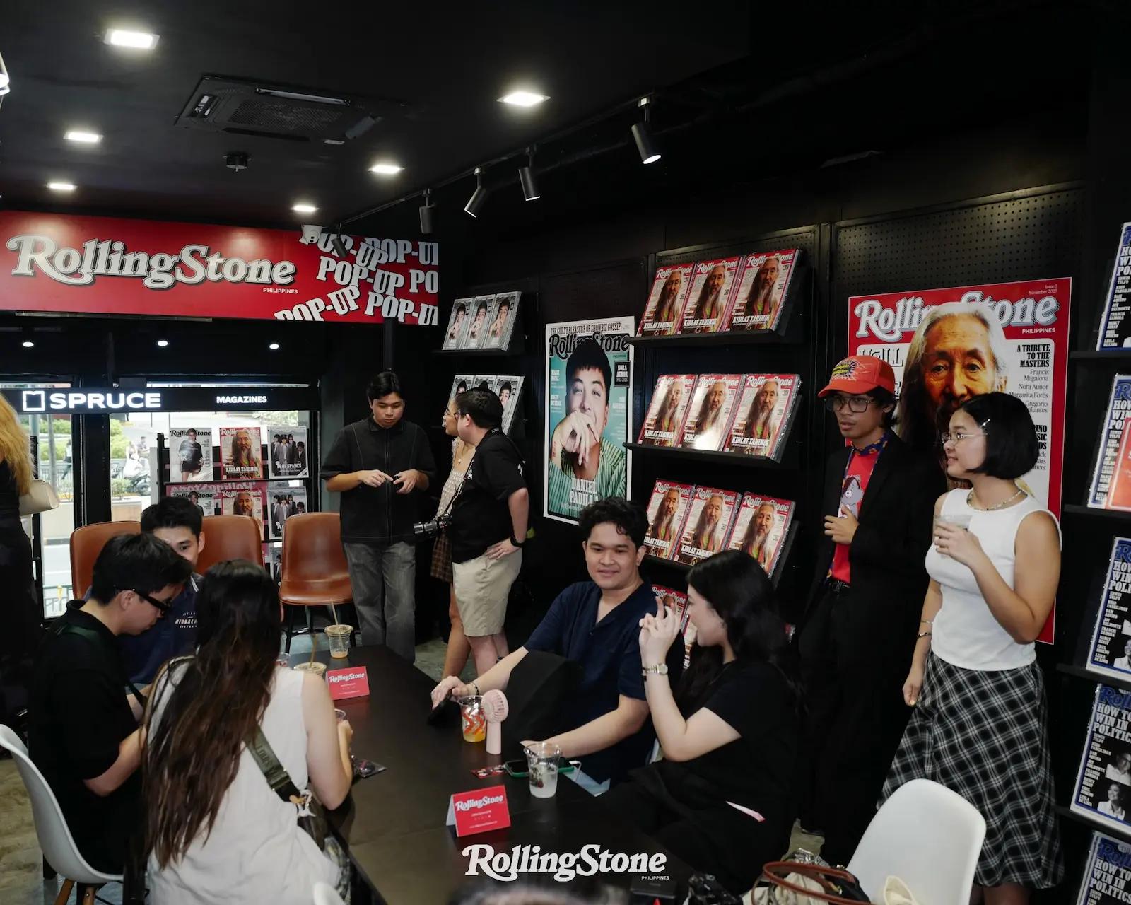 People gather around a signing table inside a Rolling Stone Philippines store, with magazine racks and large cover posters on black walls behind them.
