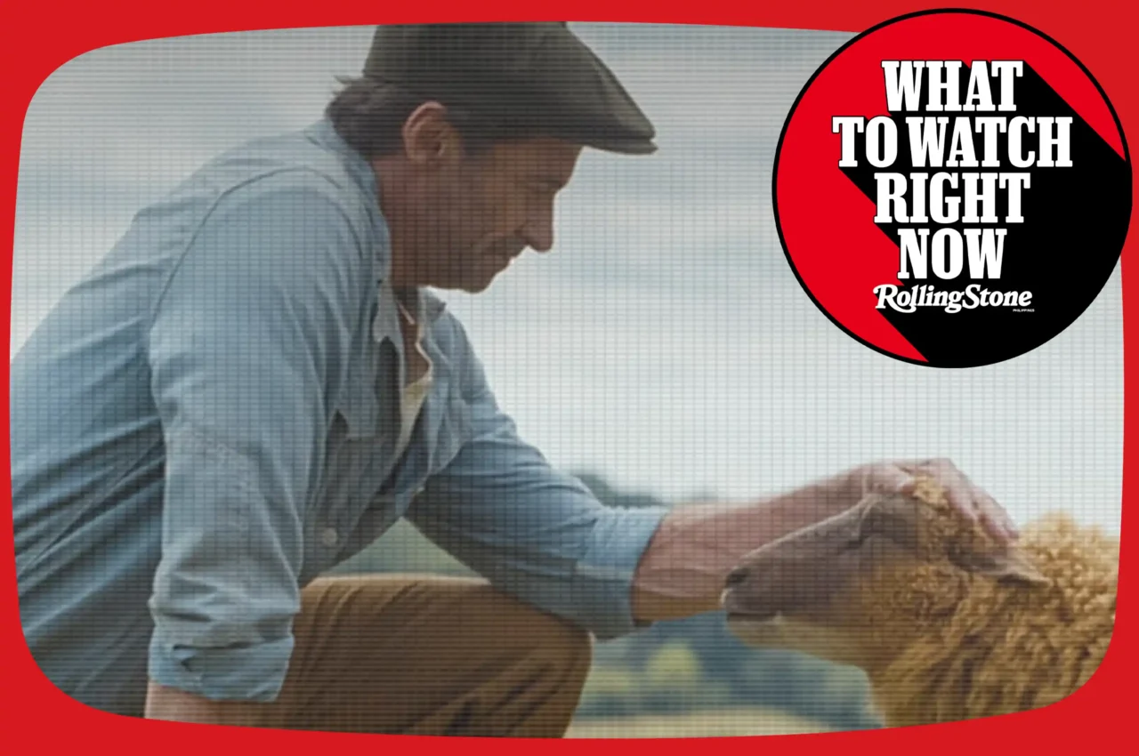 Man in a cap and denim shirt leans over a table, touching a loaf of bread, with a red banner and a 'What to Watch Right Now' Rolling Stone logo nearby
