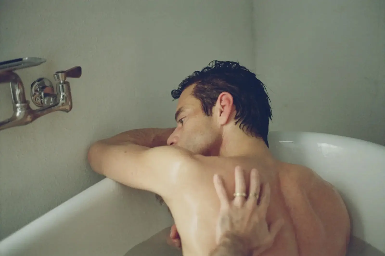 Man with wet hair resting his arm on the bathtub edge, looking to the left.