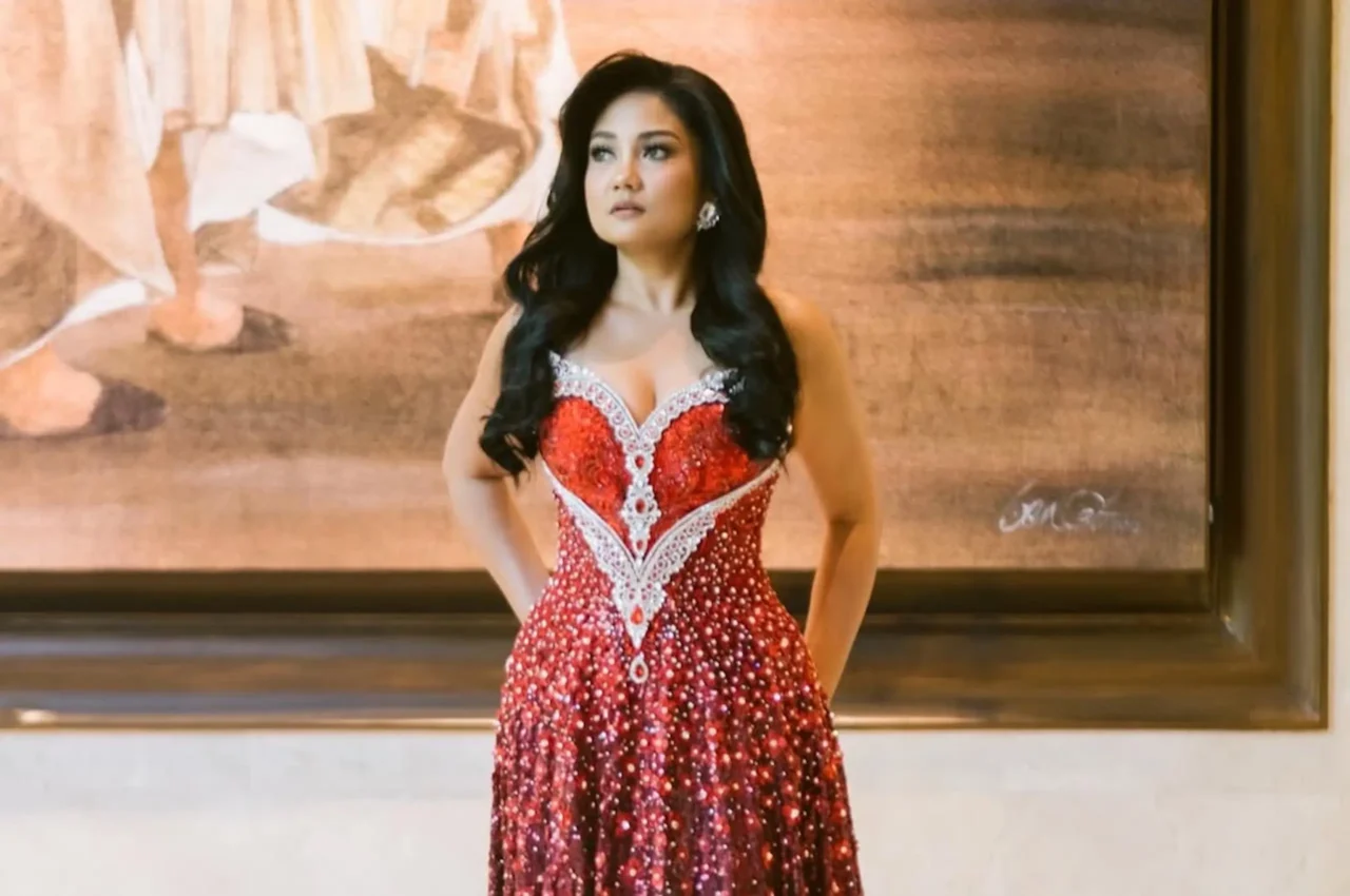 Woman in a red sequined evening gown with silver embroidery, standing on a stage against a textured backdrop.