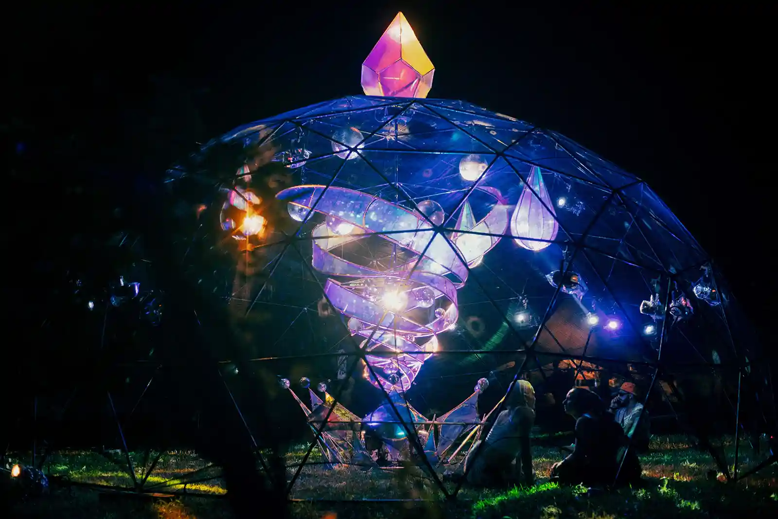 Colorful illuminated geodesic dome sculpture at night with a glowing diamond on top.